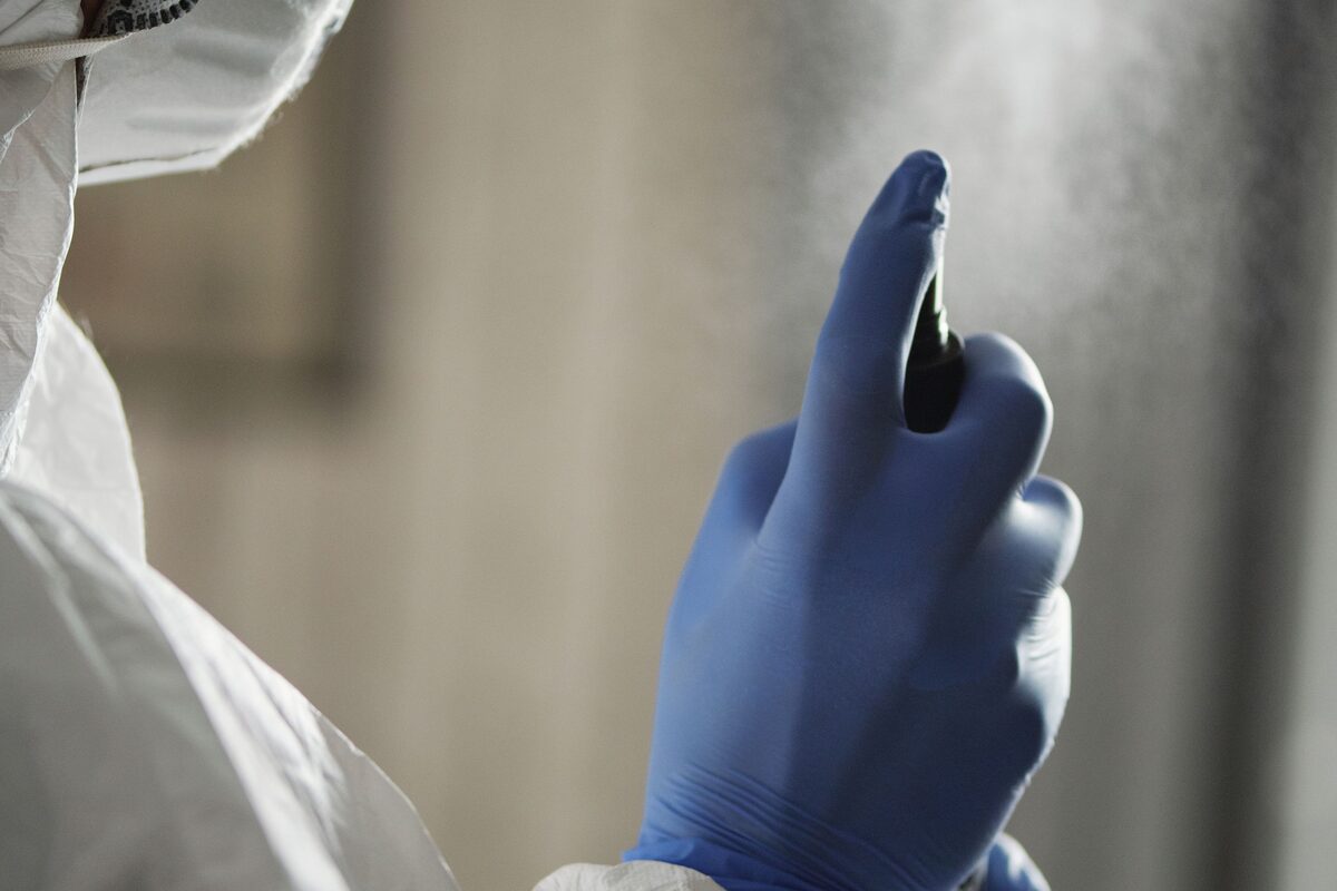 Gehandschoende hand verstuift desinfectiemiddel op een oppervlak